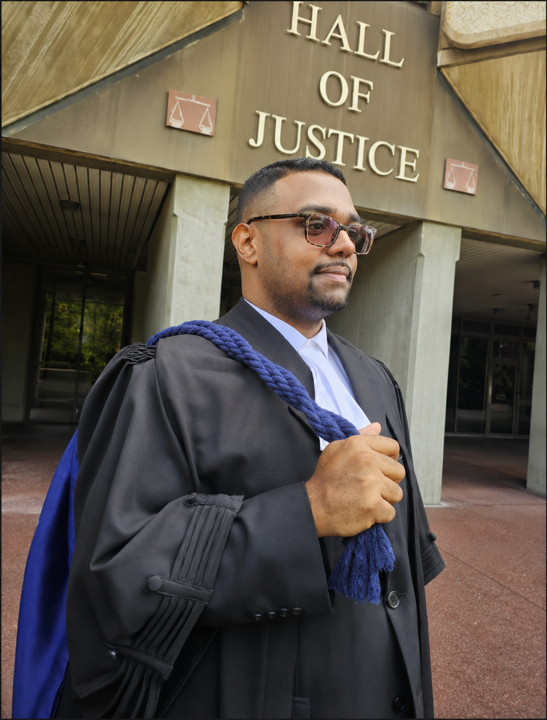 Aaron Melville in black call-to-the-bar robes with a royal-blue cord, standing before the Hall of Justice.